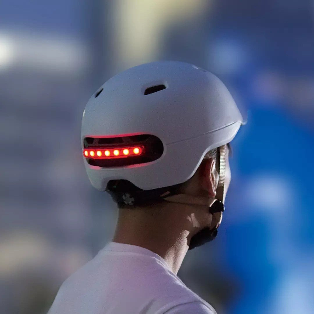 Person wearing a white helmet with red LED lights, blurred cityscape background